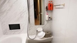 A modern bathroom with a marble wall, a digital screen, a toilet paper holder, and toiletries on a shelf.