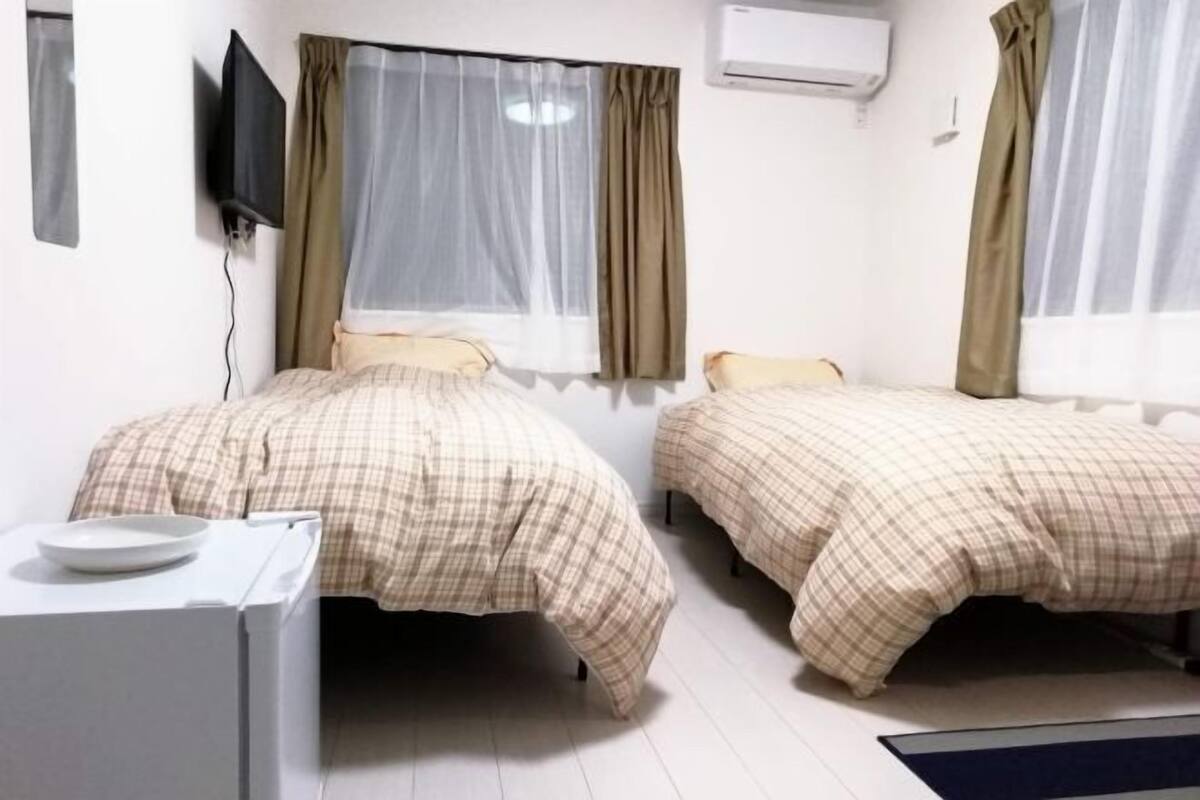 A room with two beds, a small desk, and a television mounted on the wall.