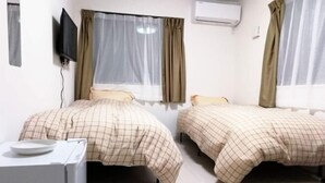 A room with two beds, a small desk, and a television mounted on the wall.