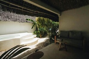 A spa area with a hot tub, a seating area with a couch and a small table, and a thatched roof structure. - Seconda Stella Romantic Hideaway (Kusini)