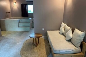 A modern room with a sofa, a small wooden stool, a woven rug, and a bathtub. - Seconda Stella Romantic Hideaway (Kusini)