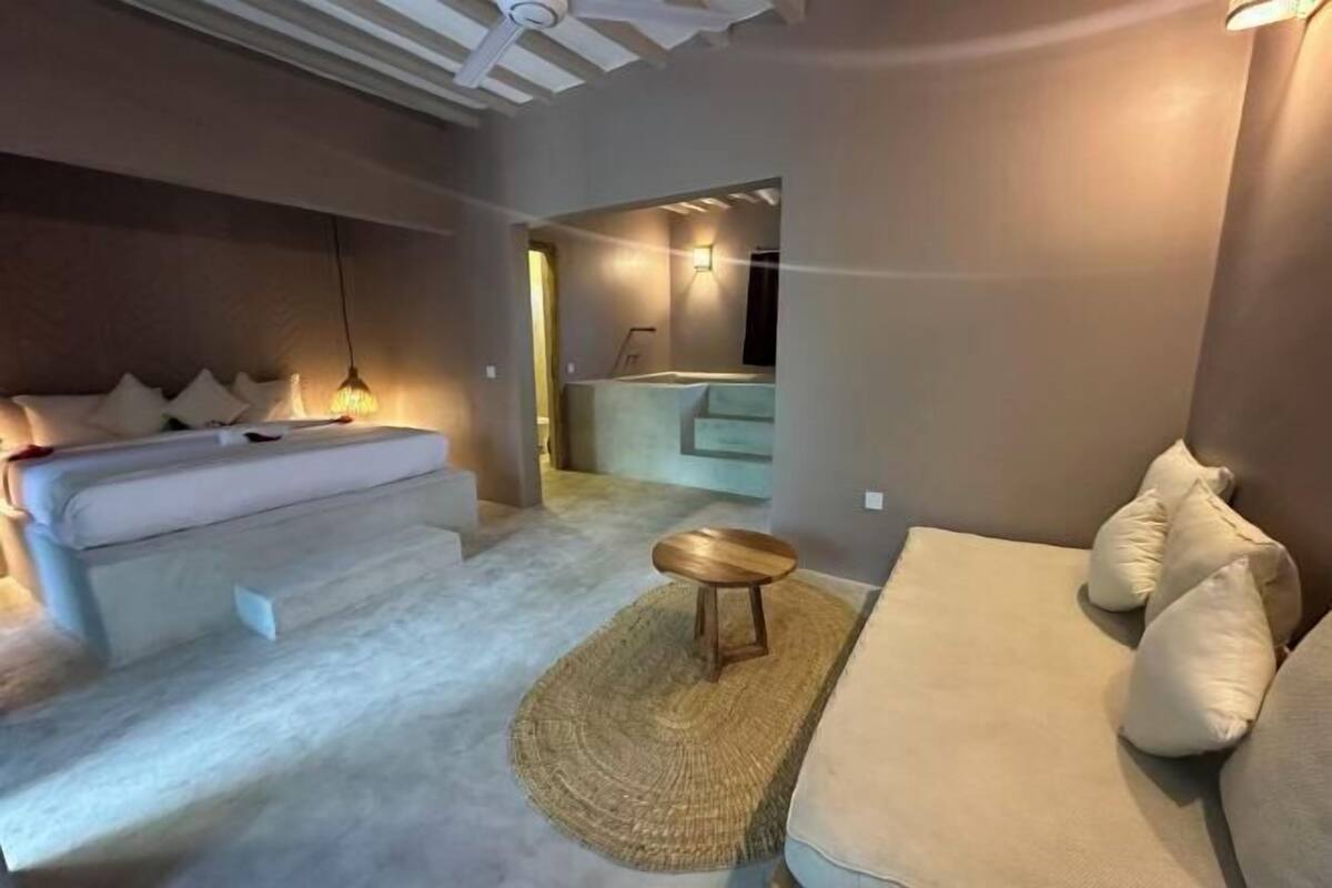 A modern bedroom with a bed, a sofa, and a small wooden stool.
