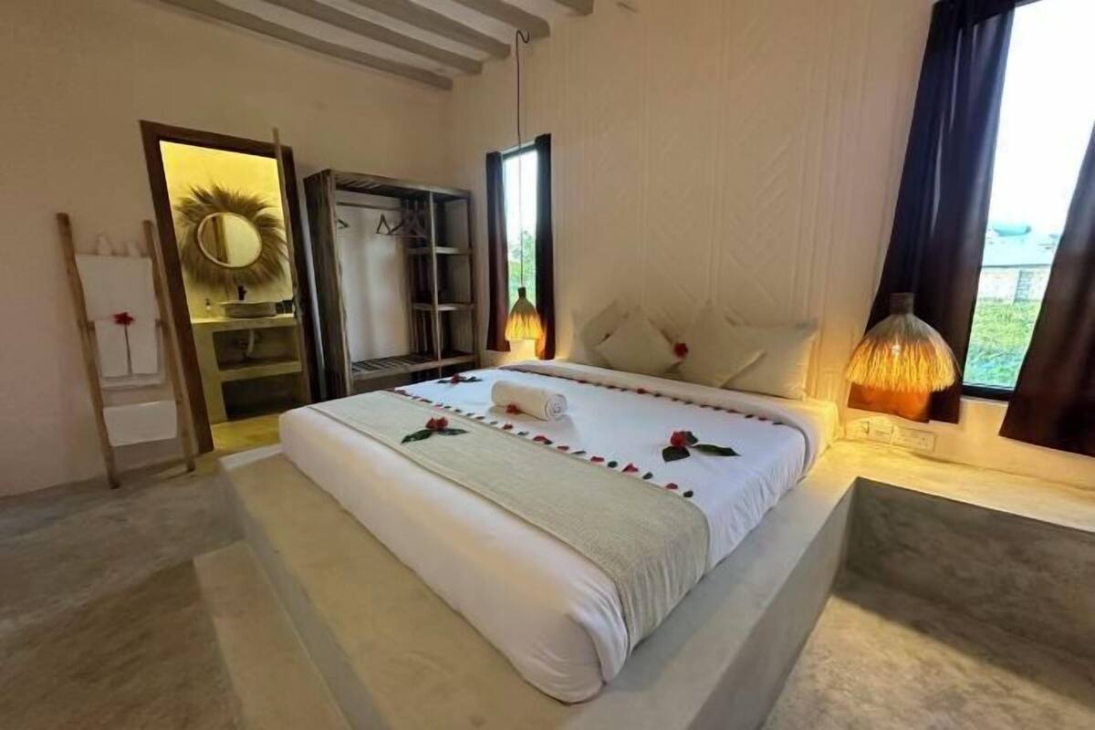 A hotel room with a bed, a wardrobe, a mirror, a window with curtains, and a lamp.