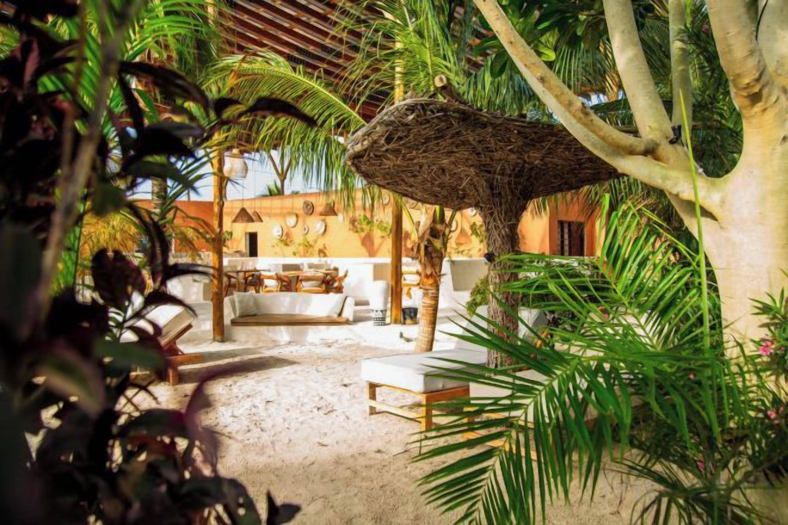 A tropical outdoor area with a thatched umbrella, lounge chairs, and a dining setup.