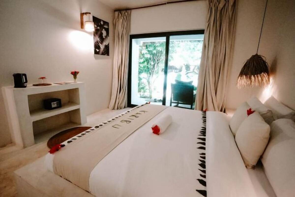 A bedroom with a bed, a desk, a chair, and a view of the outdoors.