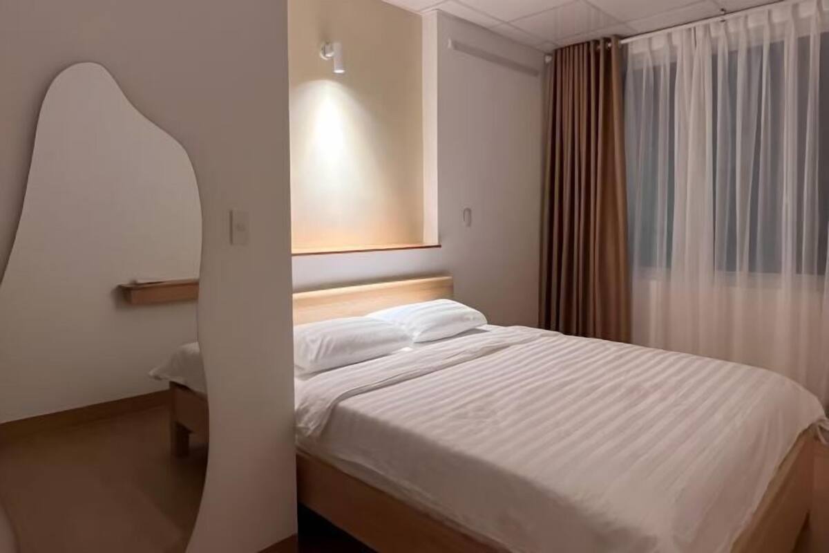 A modern hotel room with a wooden bed, a large mirror, and sheer curtains.