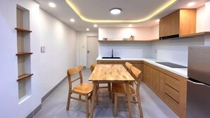 A modern kitchen with a wooden dining table and chairs, built-in wooden cabinets, and a stainless steel refrigerator. - Central, Near Airport, Dragon Bridge - Gau's House (Da Nang)
