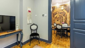 A room with a television on a wooden stand, a black chair, and a dining area with a table and chairs. - Ganbaru Tours - Flats in Galata (Istanbul)