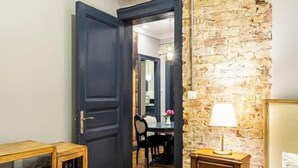 A room with a dark wooden door, a stone wall, a small wooden table with a lamp, and a bed with a white pillow. - Ganbaru Tours - Flats in Galata (Istanbul)