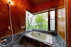 A bathroom with a stone sink, a bathtub, and a window with a view of trees. - Cottage morikaze terrace (Nasu)