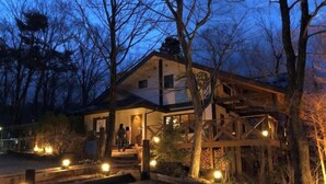 A wooden cabin with a porch, surrounded by trees and lit by ground lights. - Cottage morikaze terrace (Nasu)