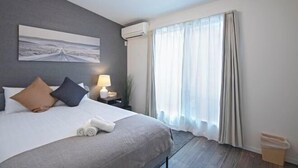 Hotelkamer met een bed, nachtkastje, lamp, airconditioning, raam met gordijnen en een wanddecoratie.