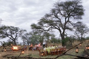 An outdoor dining area with tables and chairs, surrounded by trees, under a cloudy sky. - Kenzan Matawi Serengeti camp (Serengeti)