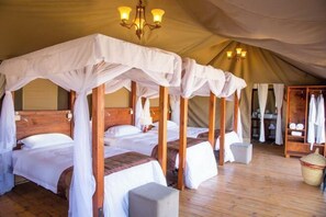 A tented accommodation with four beds, each with a canopy, wooden headboards, and a small bedside table. - Kenzan Matawi Serengeti camp (Serengeti)