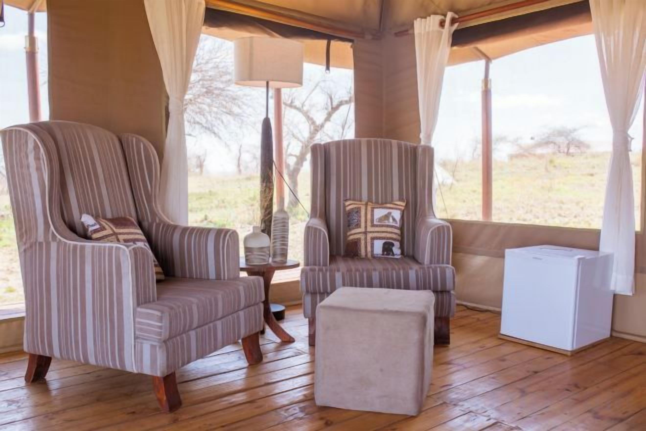 A room with two striped armchairs, a small table, a white cabinet, and a view of the outdoors.