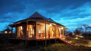 A tent-style accommodation with a covered outdoor area, steps leading to the entrance, and a view of the surrounding landscape.