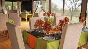A dining area with tables set for four, each with a green tablecloth, white chairs, and orange napkins.