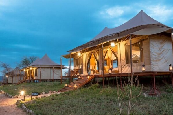 A series of tents with a wooden deck and stairs leading to the entrance, surrounded by a grassy area.