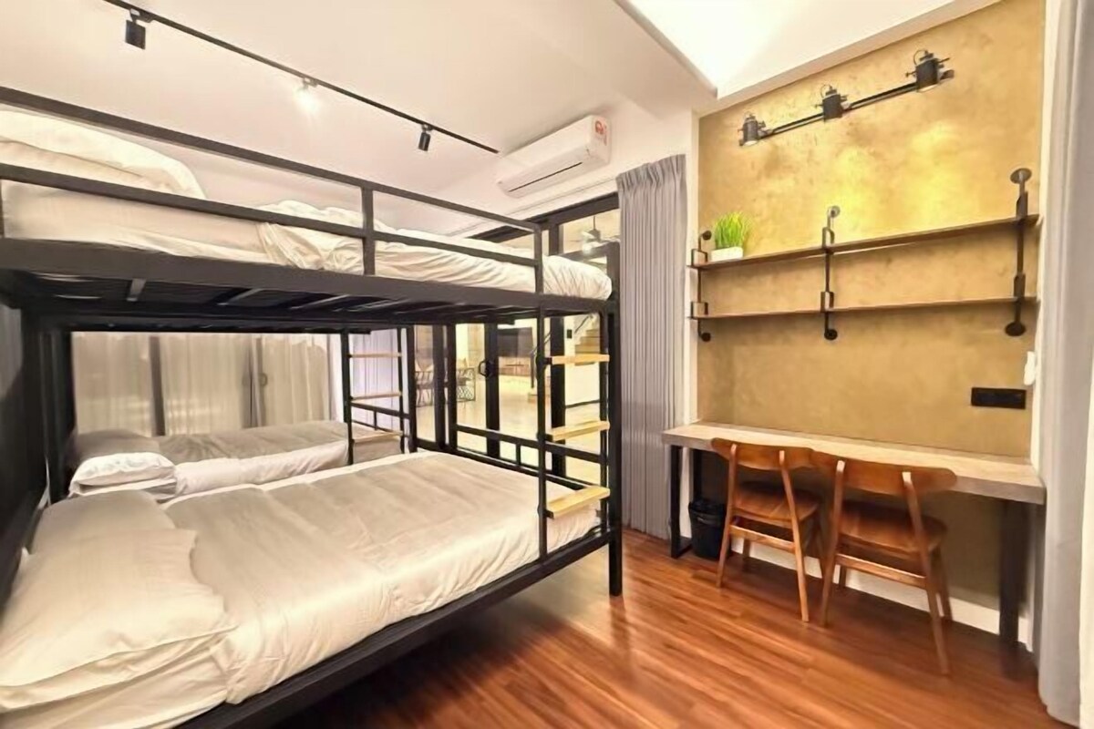 A bunk bed room with a desk and chairs, an air conditioner, and a shelf with plants.