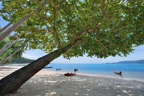 A beach with a tree providing shade, a sandy shore, and several boats in the water. - Baan Chao Lay (Koh Samui)