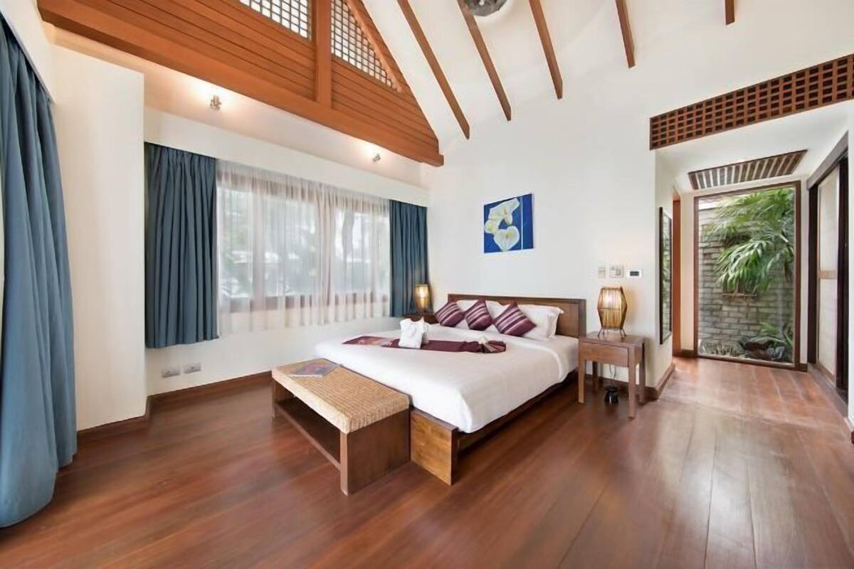 A bedroom with a wooden bed, a bench, a nightstand, and a view of greenery.