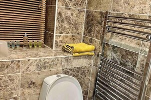 Un baño con pared de azulejos de mármol, un perchero con toallas, dispensador de jabón y un inodoro.