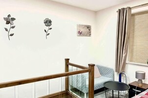 Una habitación con una cama, una mesita de noche con lámpara, una silla y una ventana con cortinas.