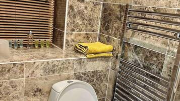 A bathroom with a toilet, a towel rack with towels, and a hand dryer.