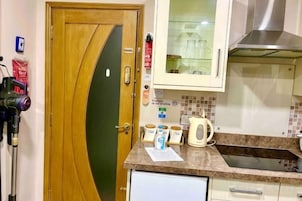Una cocina con puerta de madera, microondas, hervidor y un mueble con puertas de cristal.