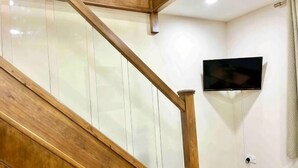 Una escalera de madera con barandillas de vidrio, un televisor montado en la pared y un enchufe.