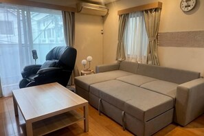 A room with a sofa, a massage chair, a small table, and a clock on the wall. - Beyond Comfort Shinjuku Okubo (Tokyo)