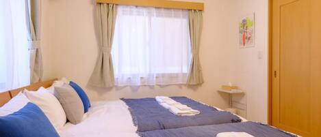 A double bed with a blue and white duvet, a bedside table with a lamp, and a window with curtains.