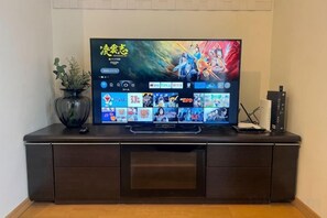 A flat-screen TV on a dark wooden cabinet with a plant beside it. - Beyond Comfort Shinjuku Okubo (Tokyo)