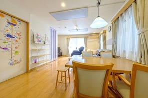A room with a dining table, chairs, a small stool, a bookshelf, and a wall with a colorful mural. - Beyond Comfort Shinjuku Okubo (Tokyo)