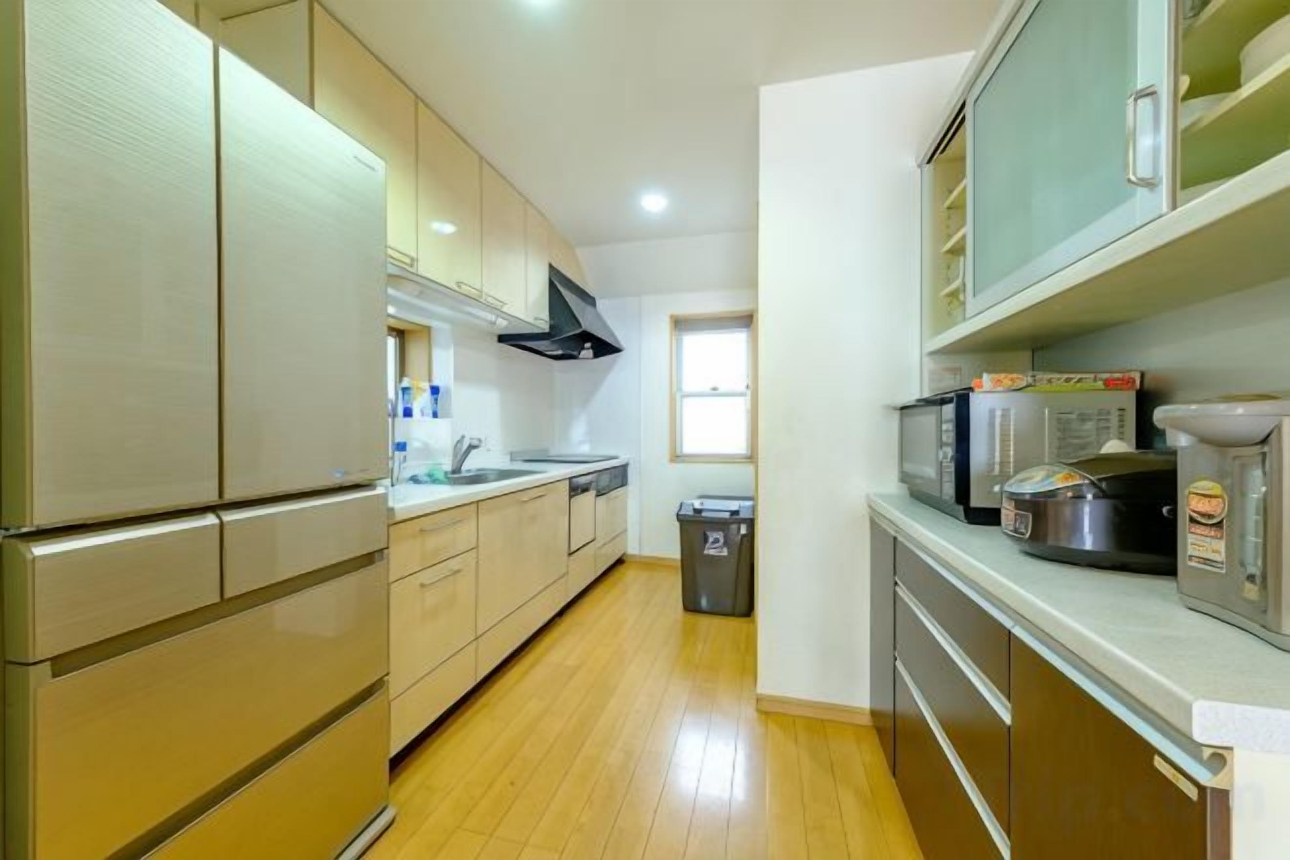 A kitchen with stainless steel appliances, wooden cabinets, and a trash bin.
