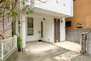 A residential building with a tiled exterior, a visible door, and a small outdoor area with a concrete floor. - Beyond Comfort Shinjuku Okubo (Tokyo)