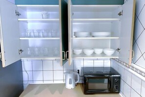 A kitchen with open cabinets, a kettle, a microwave, and shelves with bowls and glasses. - GUEST HOUSE X (Tokyo)