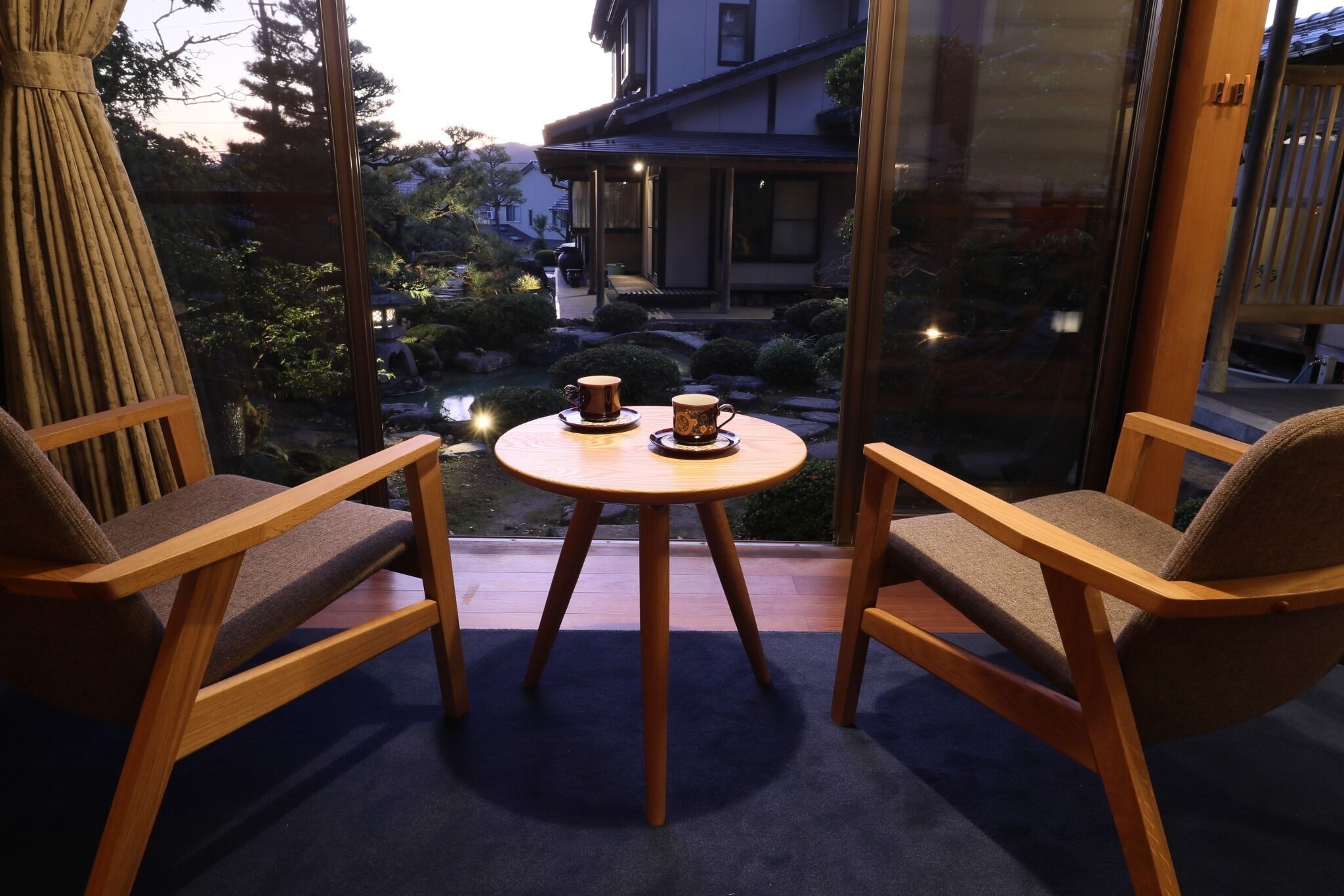 A balcony with two wooden chairs and a small round table, each with a cup and saucer.