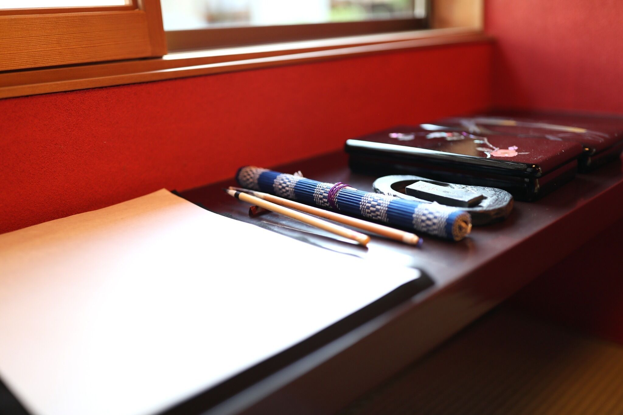 Un escritorio con un cuaderno, un bolígrafo, unos palillos y un estuche negro pequeño.