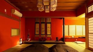Een kamer met een bed, een klein tafeltje, een stoel, een raam met zonwering en een airconditioner aan de muur.