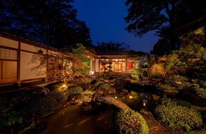 En traditionel japansk have i skumringen med en koi-dam, sten og en træbygning med skydedøre.