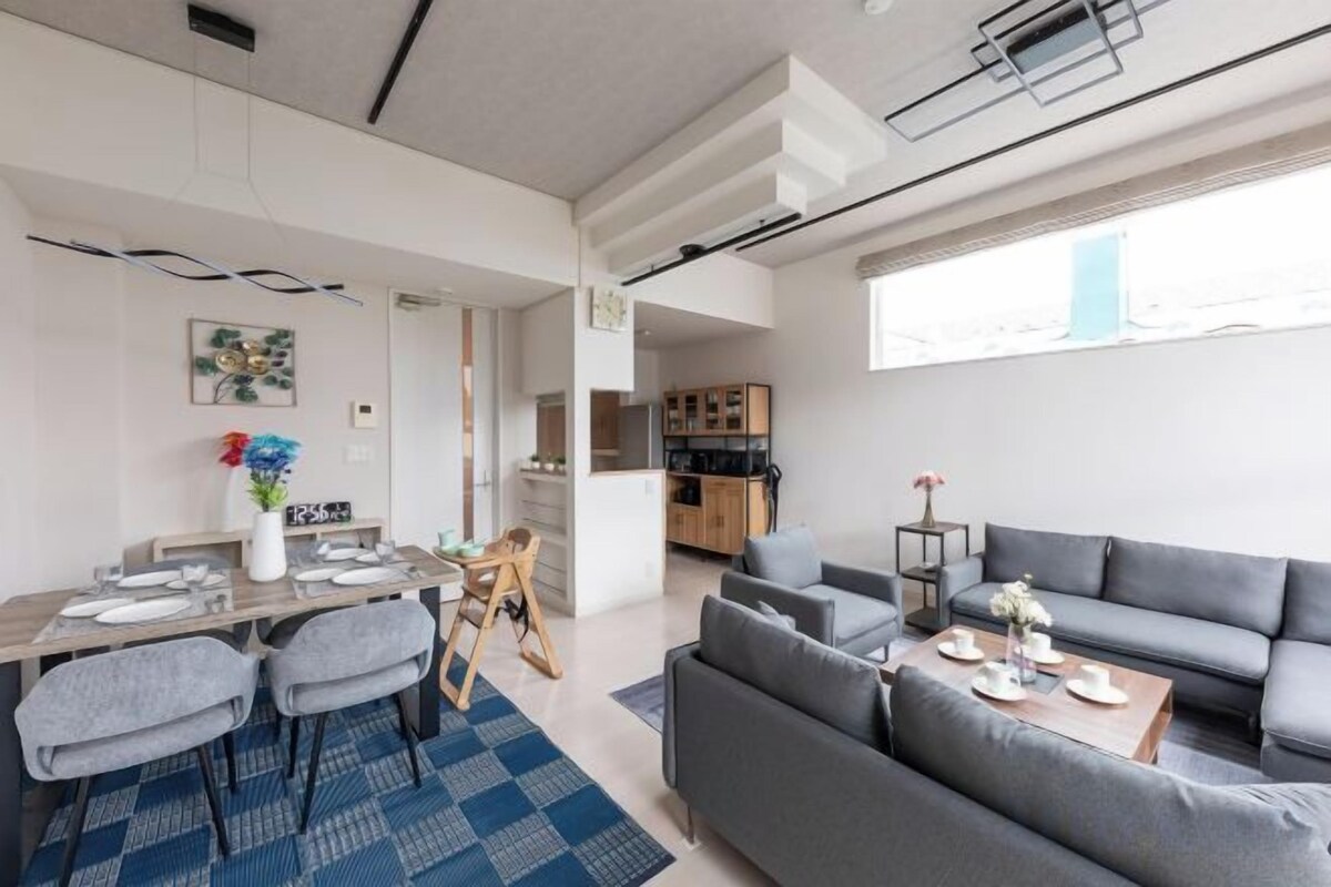 A modern living room with a sofa, dining table, and chairs. There is a kitchen area in the background.
