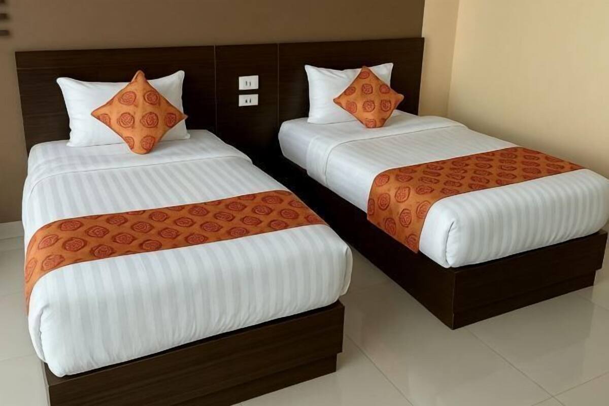 Dos camas individuales con cabeceros a juego, ropa de cama blanca con diseños anaranjados y una base de cama marrón.