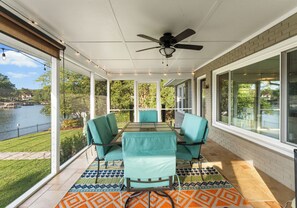A covered patio with a table and chairs, large windows, and a view of a lake. - Dock, Hot Tub & Kayaks on Lake Norman | Lakeside Gem by AvantStay (Denver)