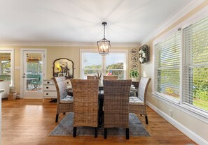 A dining area with a table and chairs, a chandelier, and large windows with blinds. - Dock, Hot Tub & Kayaks on Lake Norman | Lakeside Gem by AvantStay (Denver)