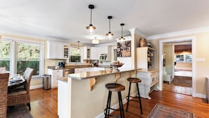 A modern kitchen with a central island, bar stools, pendant lighting, and a large clock on the wall.