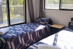 A hotel room with two beds, a small table, and large windows. - Holiday apartment (Nadi)