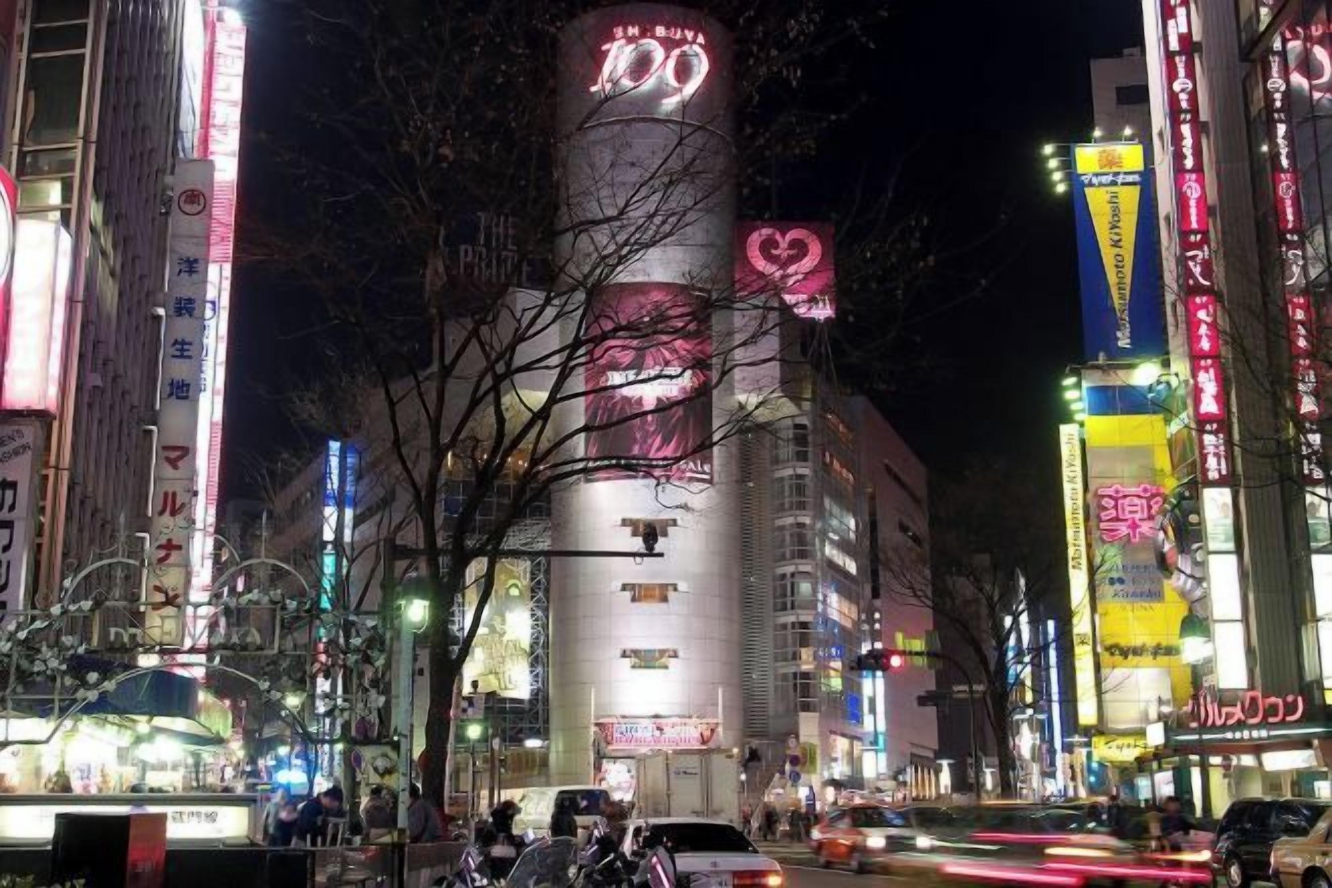 Una calle urbana concurrida de noche, con letreros y edificios iluminados.