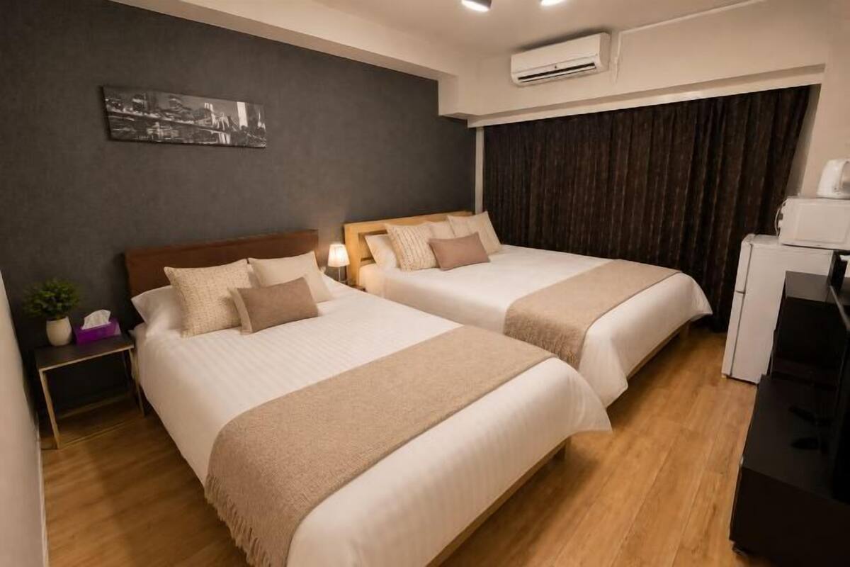 Habitació d'hotel amb dos llits, un escriptori, aire condicionat i una obra d'art penjada a la paret.