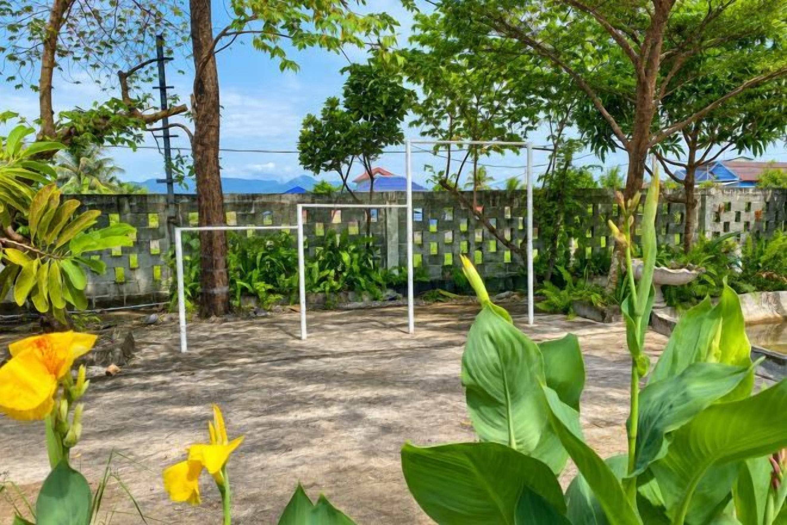 Un espace extérieur clos, doté de poteaux de but, entouré de verdure et d’arbres.